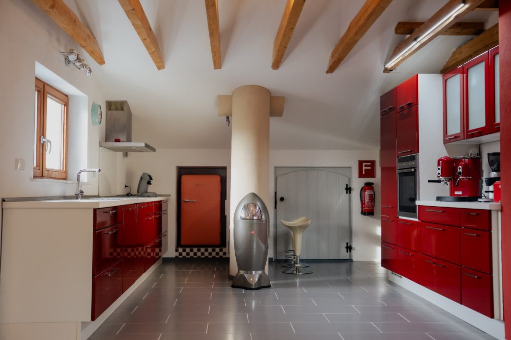 Moderne Küche mit roten Möbeln, weißen Wänden und Holzdeckenbalken.