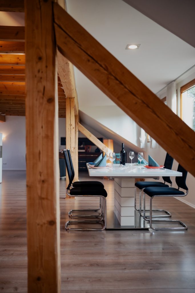 Essbereich mit Tisch und Stühlen unter schrägen Holzbohlen in modernem Raum.