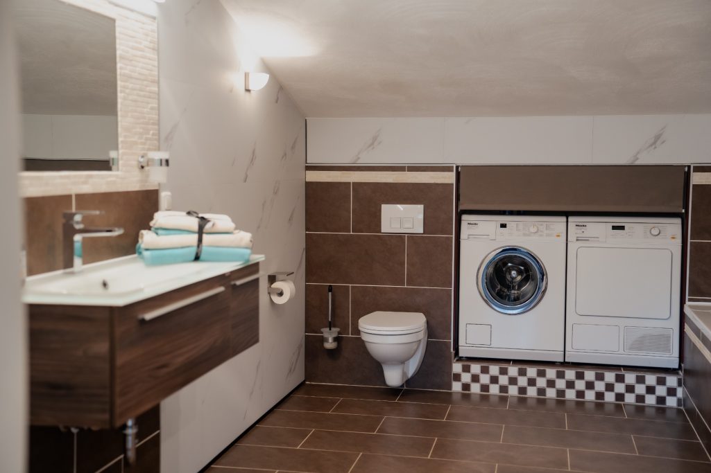 Badezimmer mit Waschmaschine, Trockner, WC und modernem Waschbecken.