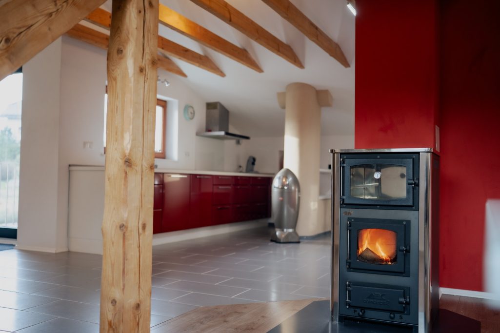 Moderne Küche mit roter Wand, Holzstützen und einem Kaminofen.