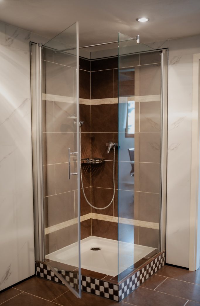 Moderne Dusche mit gläserner Abtrennung und braunen Fliesen.