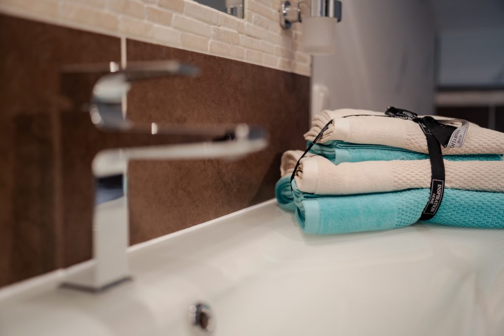 Badezimmer mit einem Wasserhahn und gestapelten Handtüchern in verschiedenen Farben.